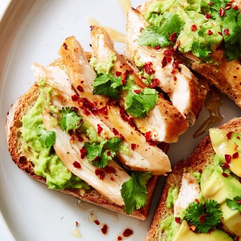 Golden grilled chicken slices arranged over creamy smashed avocado on toasted sourdough, drizzled with honey and sprinkled with red chili flakes for a sweet-spicy finish.