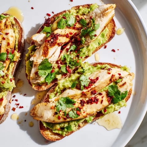 Freshly mashed avocado with lemon juice spread thickly on crusty bread, topped with smoky paprika chicken and a vibrant garnish of herbs.