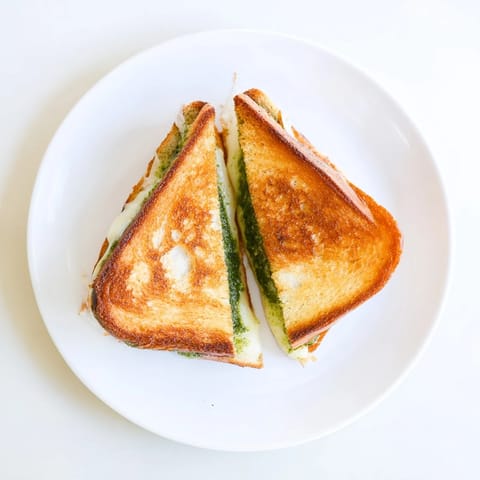 A close-up of sourdough pesto grilled cheese with crispy edges and melted mozzarella and cheddar blend.  