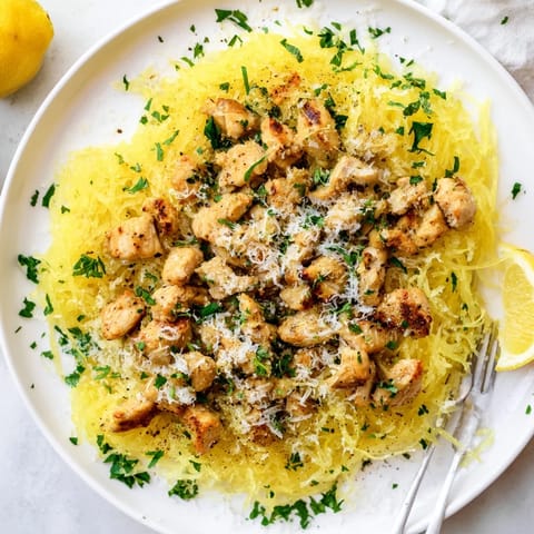 Savory lemon garlic chicken pieces nestled in roasted spaghetti squash strands, served with a bright lemon wedge for extra zest.