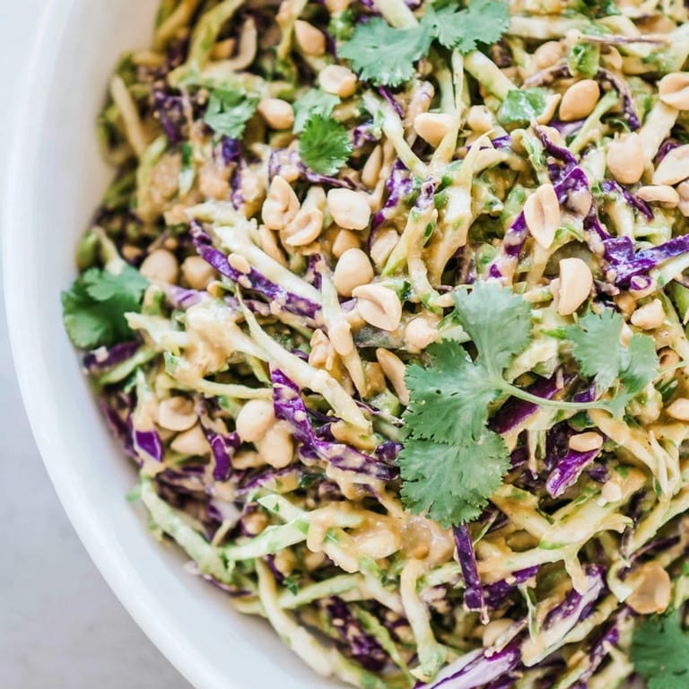 Freshly tossed Crunchy Thai Peanut Salad in a white bowl, garnished with cilantro, sesame seeds, and lime wedges for a zesty finish.