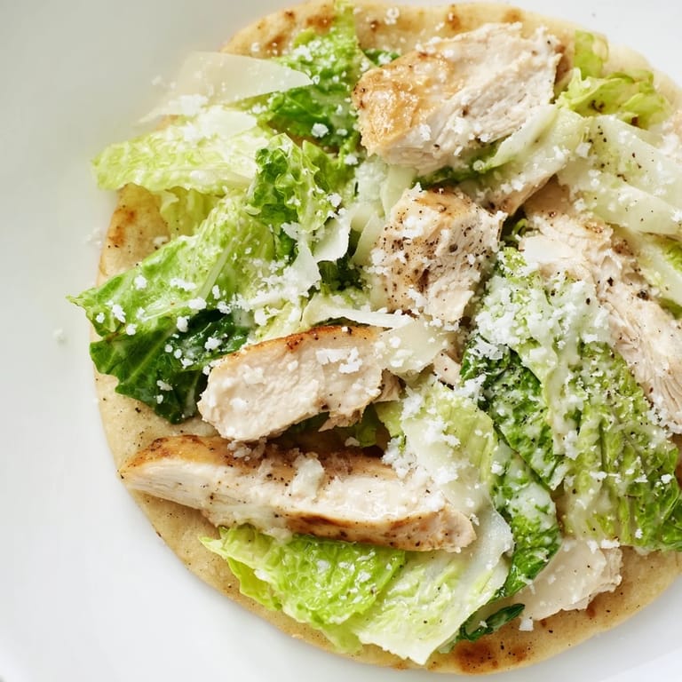 A close-up view of Chicken Caesar Flatbread with fresh greens, parmesan, and ripe cherry tomatoes.  