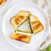 Golden-brown sourdough pesto grilled cheese slices on a wooden board, oozing melted cheese and aromatic basil.  